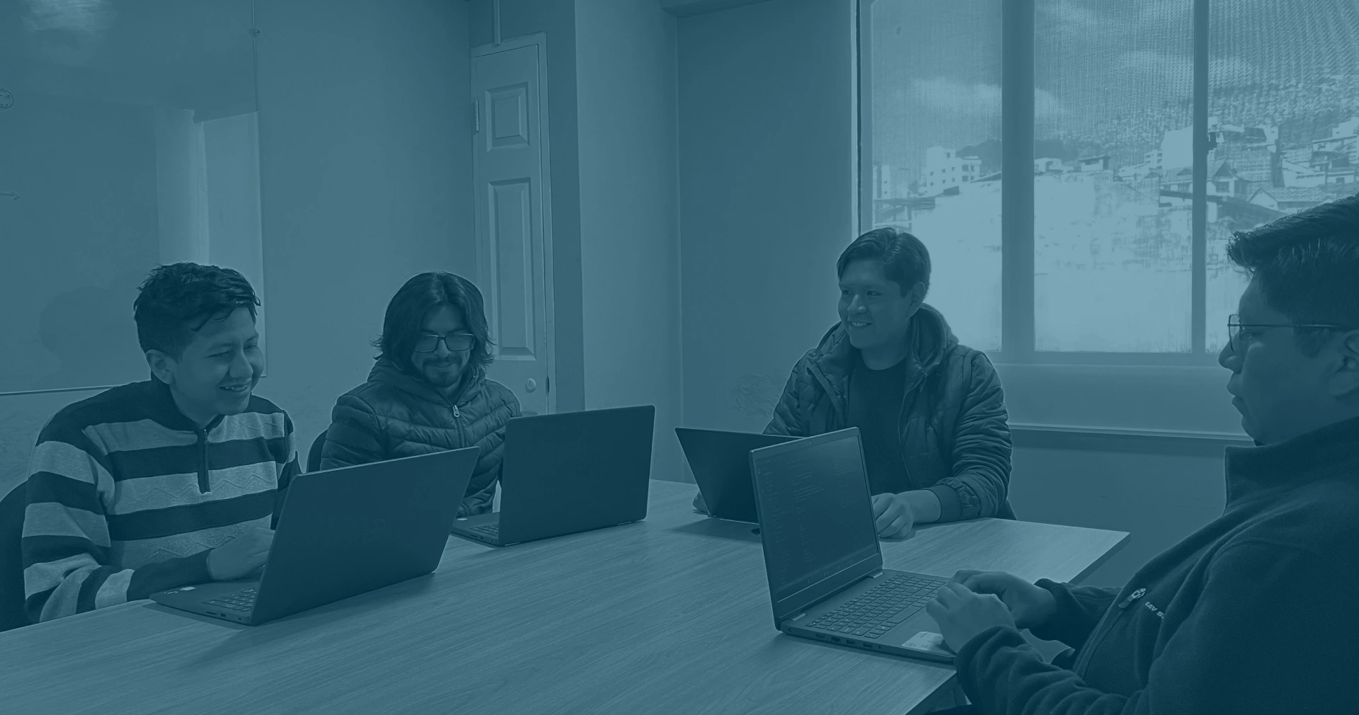 A group of people sitting around a table, each using laptops in an indoor office setting