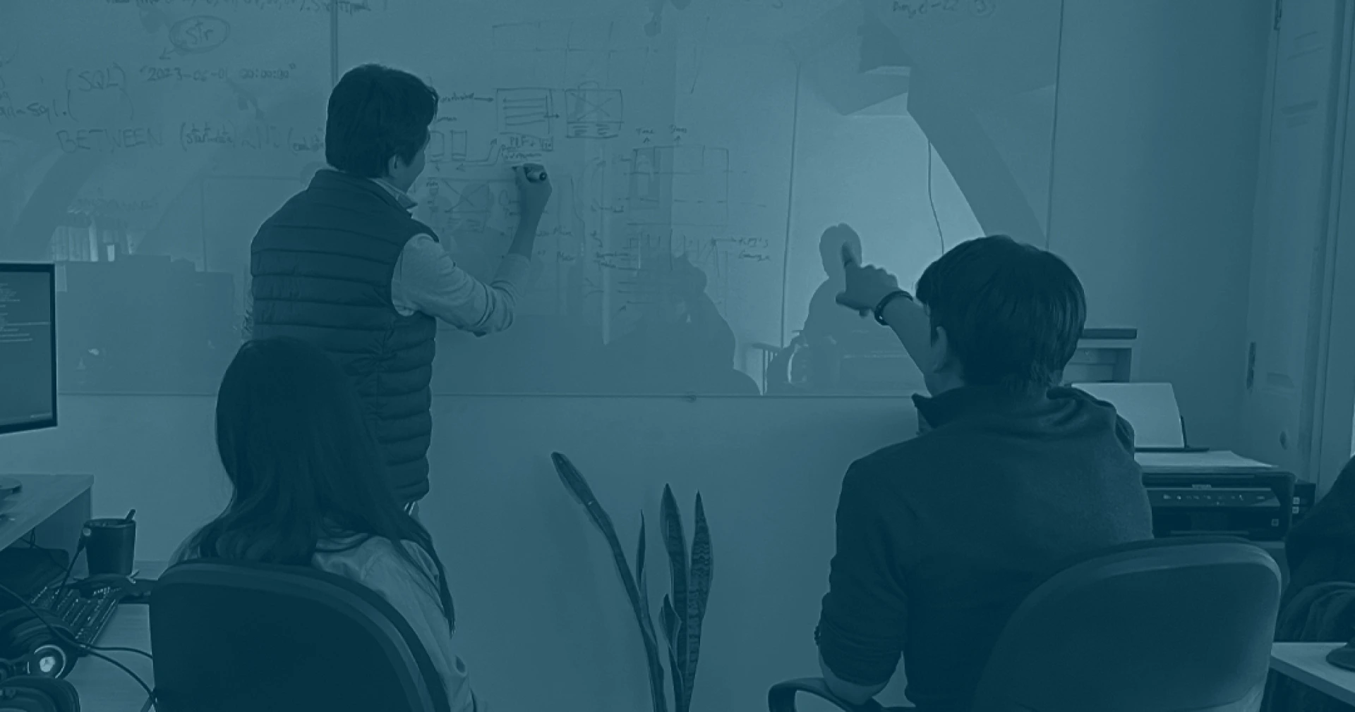 A group of people gathered around a whiteboard, writing and discussing ideas in an indoor setting